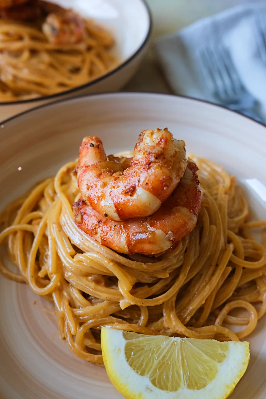 Close-up of creamy aligue pasta topped with sautéed shrimp, with a jar of crab paste in the background.