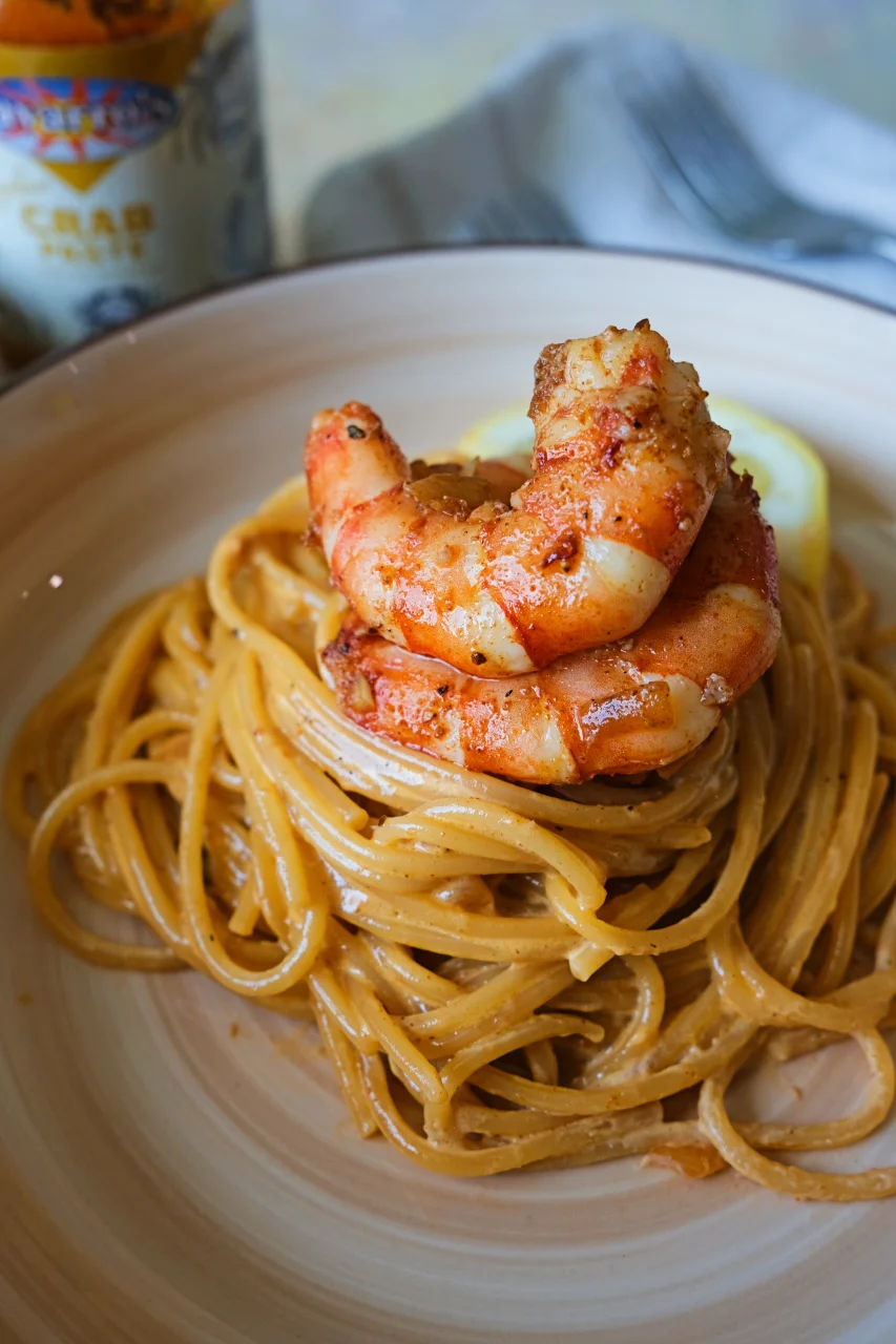 Aligue pasta with shrimp in a creamy crab paste sauce, served on a plate with crab paste in the background.