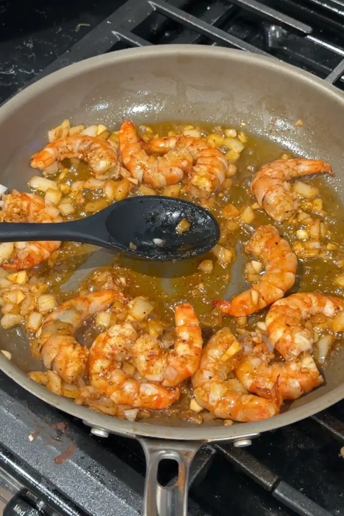Seasoned shrimp sautéing with onion and garlic until pinkish-orange and cooked through