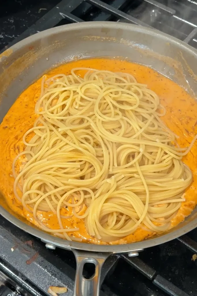 Cooked spaghetti added to the creamy aligue sauce before tossing to coat.