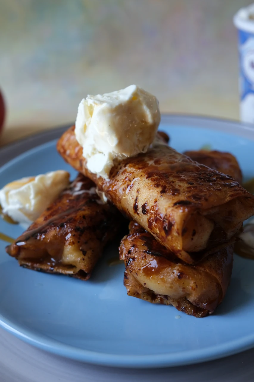 Caramelized apple turon stacked on a blue plate and topped with vanilla ice cream.