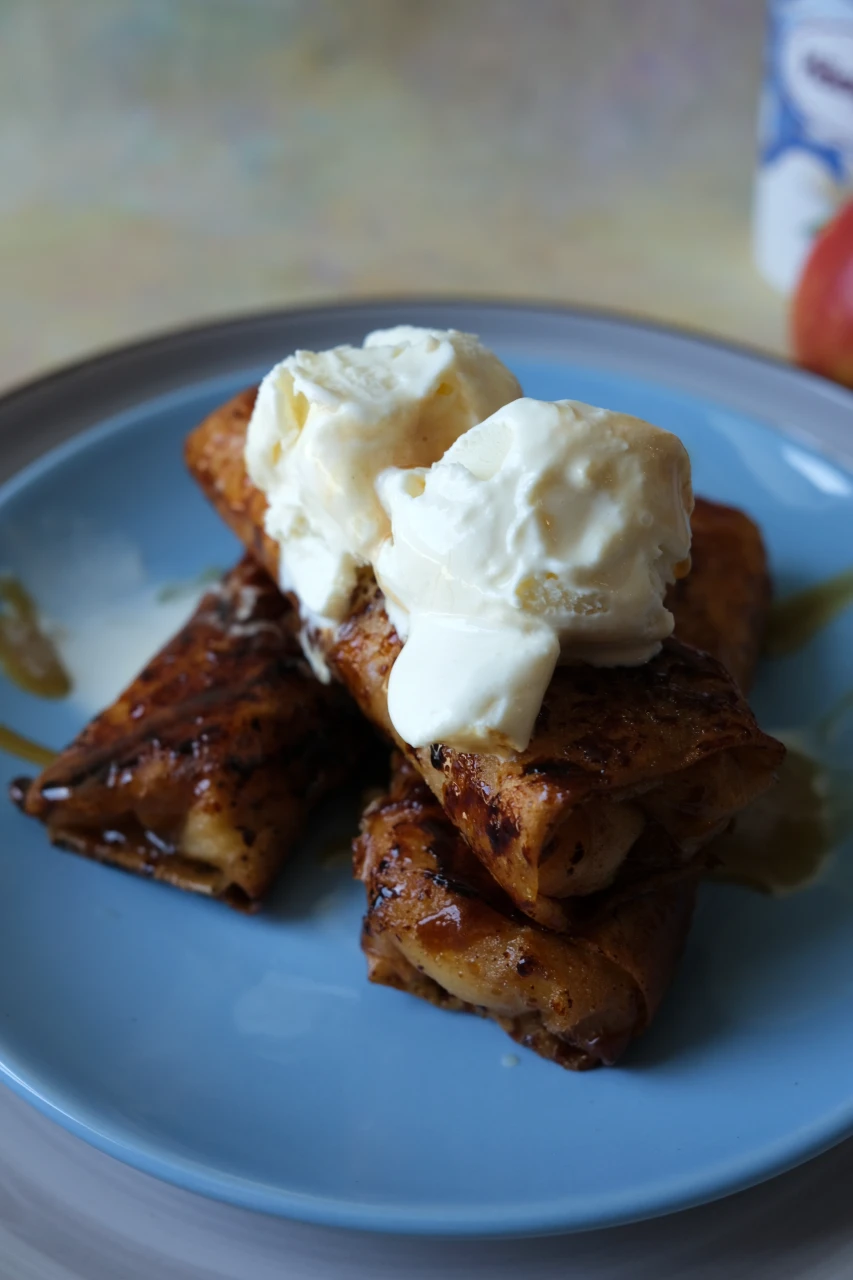 Crispy apple turon topped with scoops of vanilla ice cream and caramel sauce.