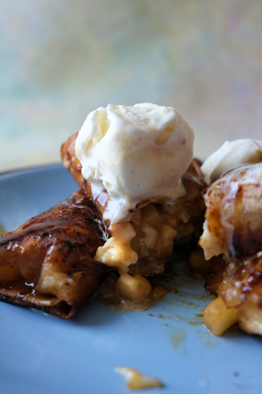 Apple turon cut open to show the cinnamon apple filling, topped with melting vanilla ice cream.