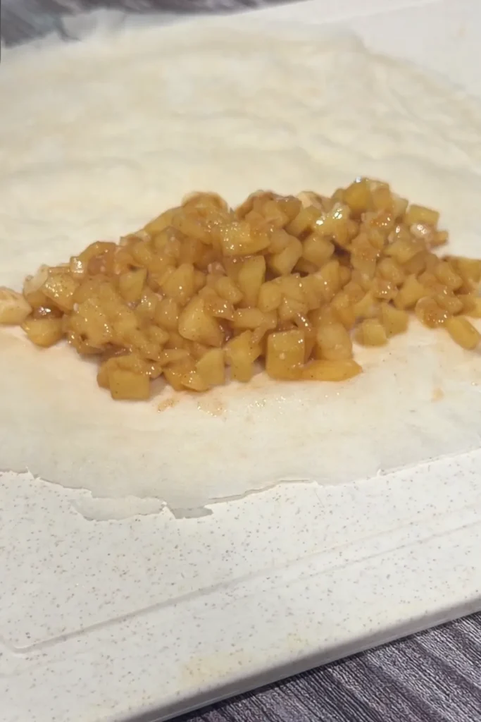 Cooked cinnamon apple filling spooned onto a round lumpia wrapper.