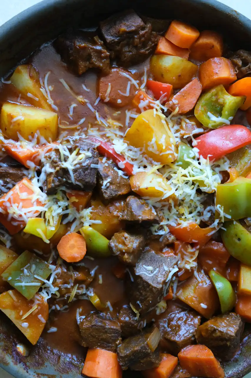 Beef kaldereta with tender beef, potatoes, carrots, bell peppers, and shredded cheese in a tomato sauce.