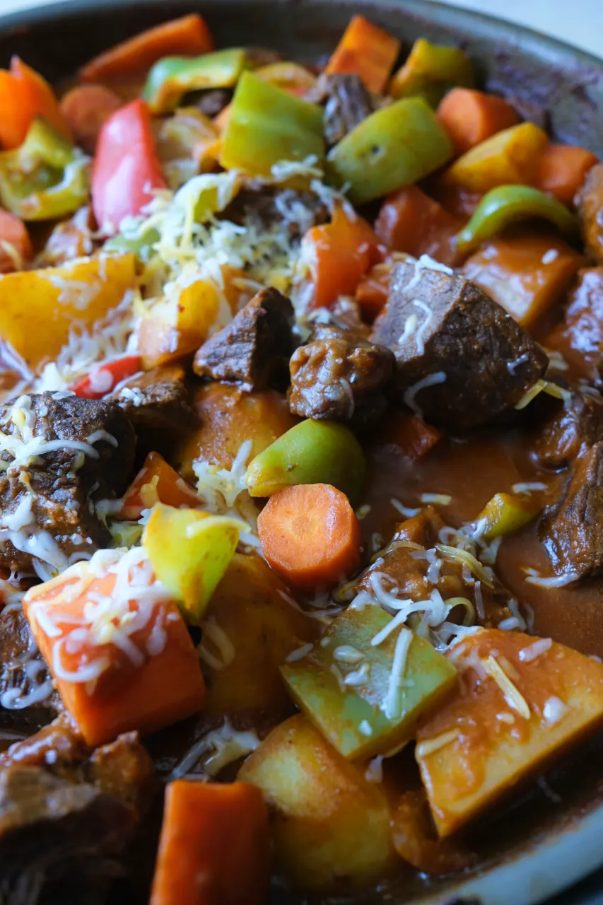Beef kaldereta with chunks of beef, potatoes, carrots, and red and green bell peppers in a thick tomato sauce.
