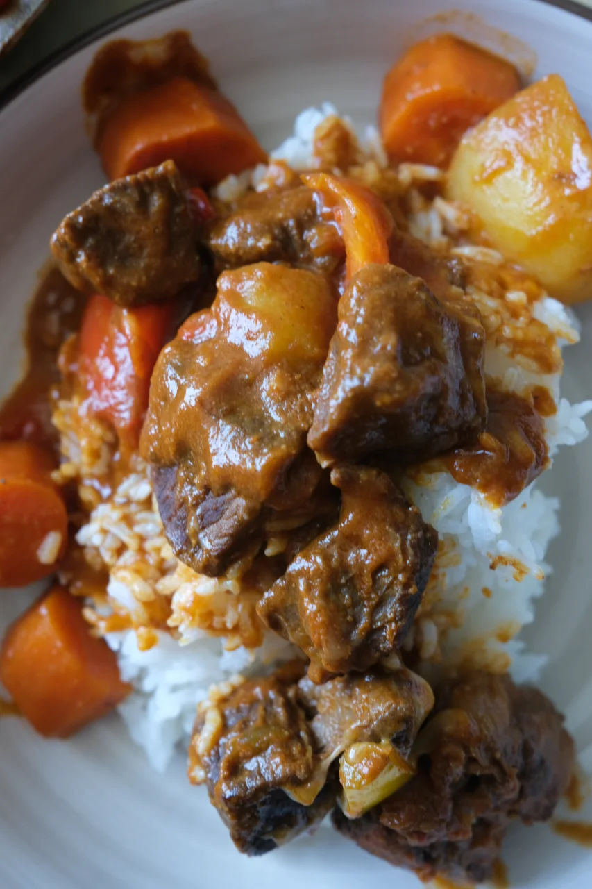 Plate of beef kaldereta over white rice with tender beef, carrots, potatoes, and tomato sauce.