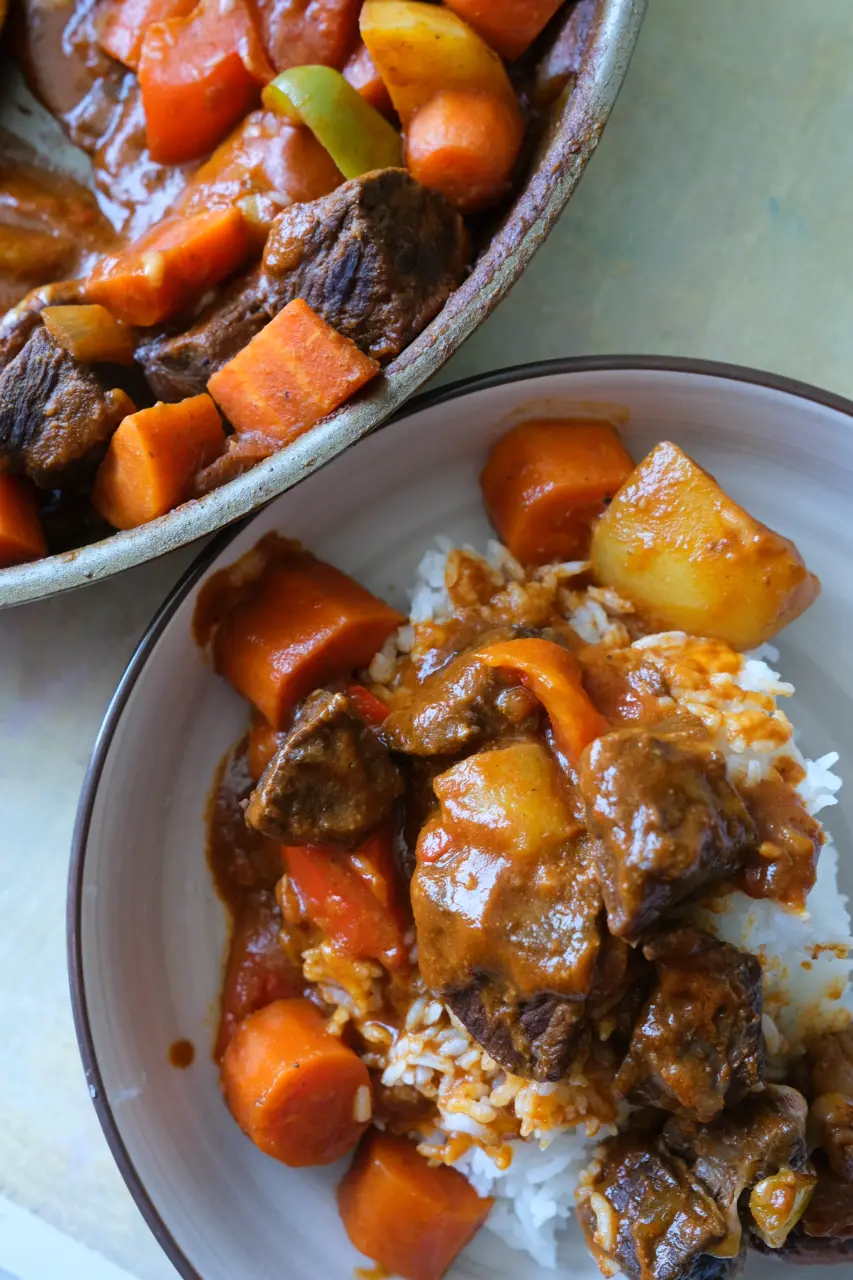 Filipino beef kaldereta served with white rice, with the remaining beef stew in a pan.