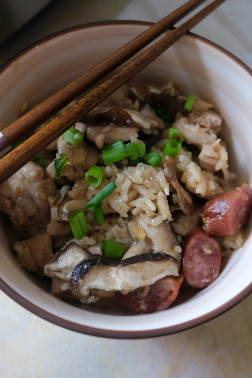 Close-up of claypot chicken rice with tender chicken, Chinese sausage, shiitake mushrooms, and green onions.