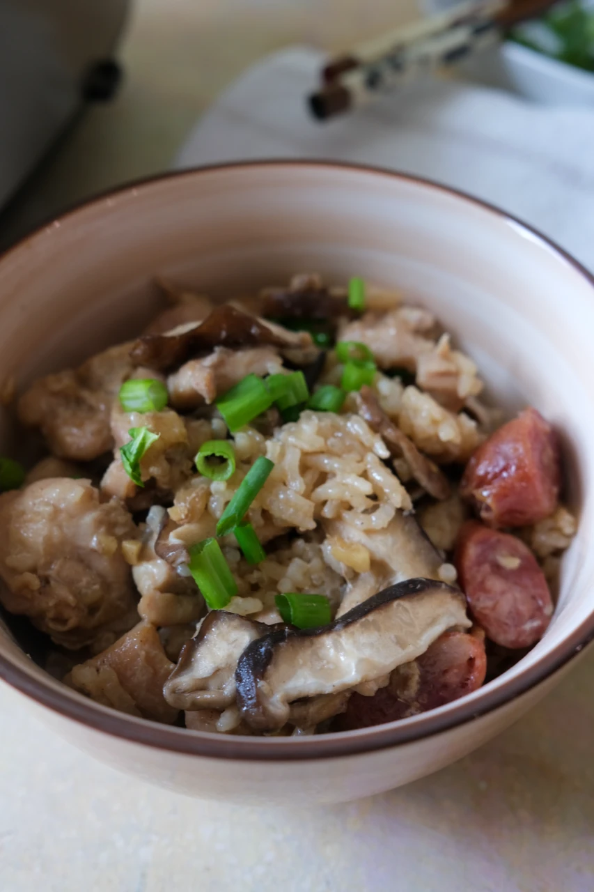 Bowl of rice cooker claypot chicken rice served with Chinese sausage, shiitake mushrooms, and green onions.