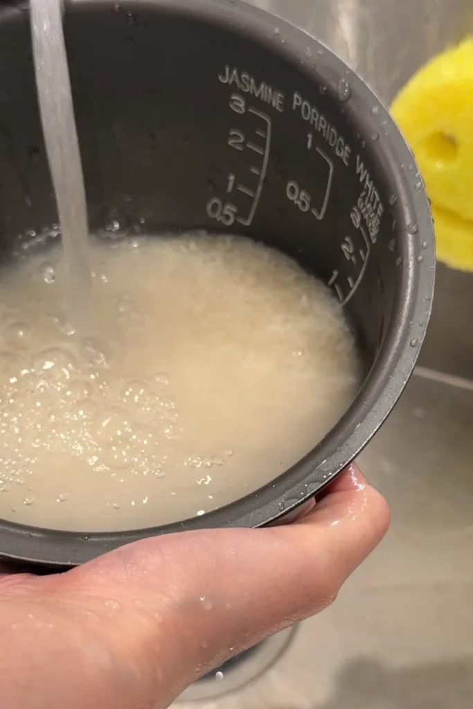 White rice being rinsed with water in a rice cooker pot.
