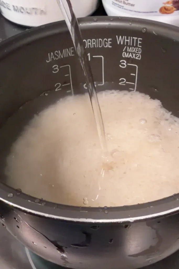 Water being added to rinsed white rice in the rice cooker pot.