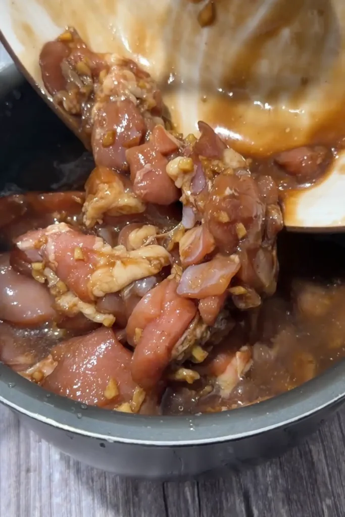 Marinated chicken and marinade being added to rice in the rice cooker.