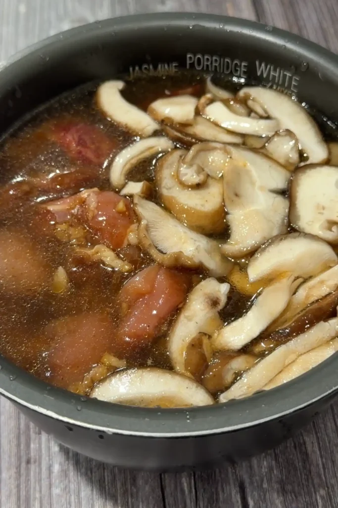 Sliced shiitake mushrooms and Chinese sausage layered over marinated chicken and rice in the rice cooker.
