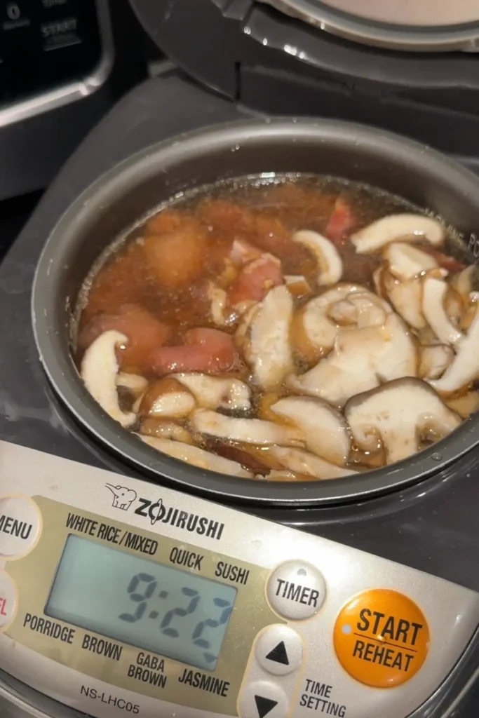 Claypot chicken rice cooking with chicken, Chinese sausage, and shiitake mushrooms in a rice cooker.
