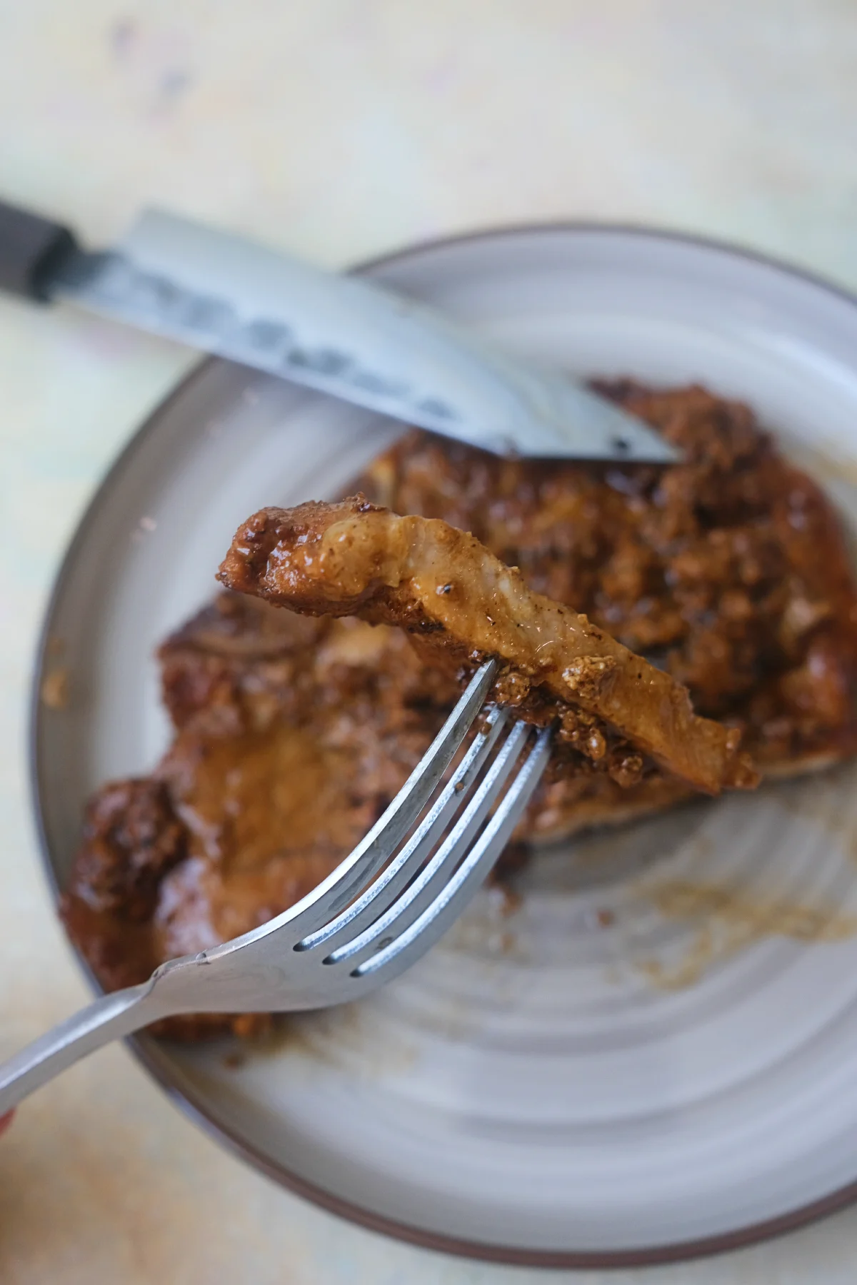 Tender slice of pork chop held on a fork with creamy pork chops in the background.