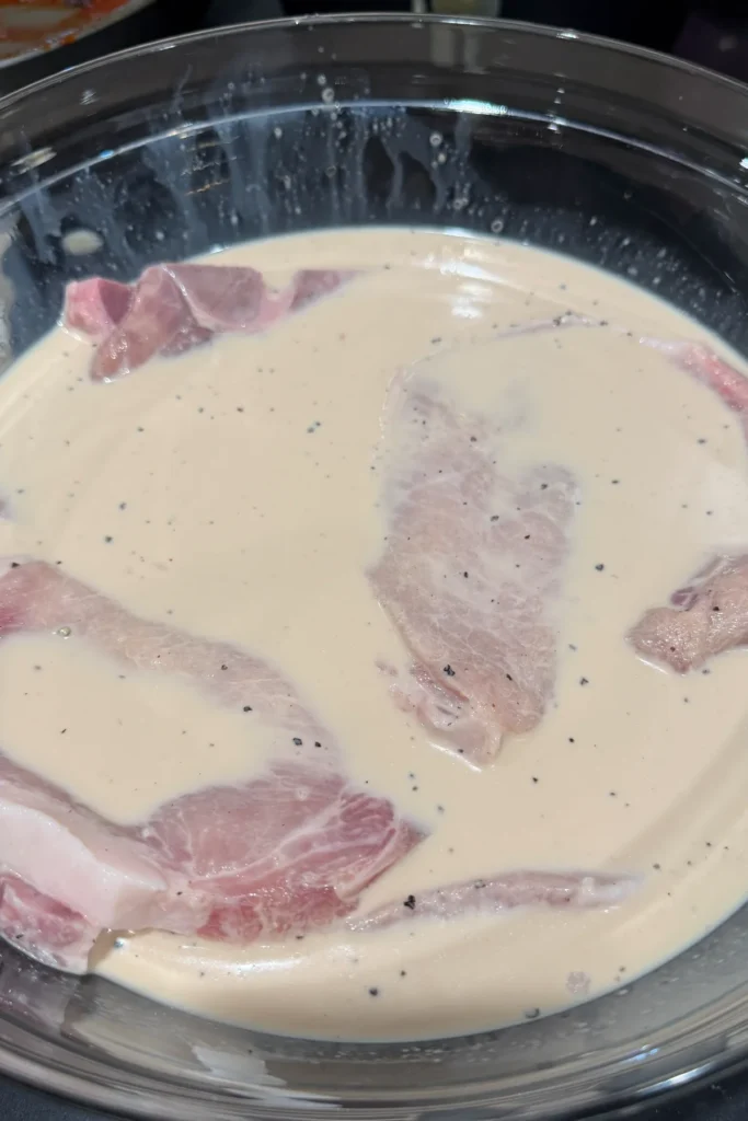 Raw pork chops marinating in evaporated milk and savory seasonings.