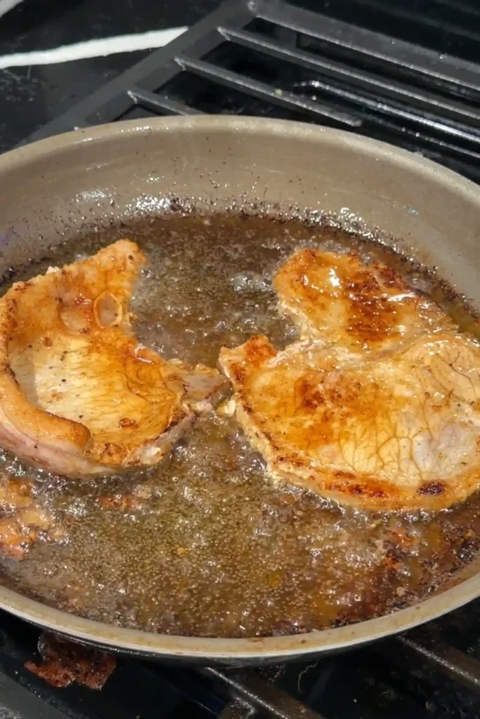 Golden-brown pork chops searing in a skillet before adding the milk marinade.