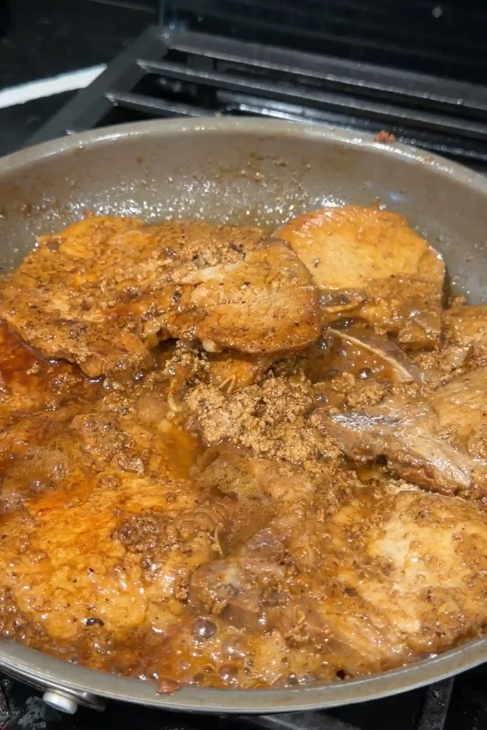 Pork chops cooking in the reduced milk marinade with savory curds forming around them.