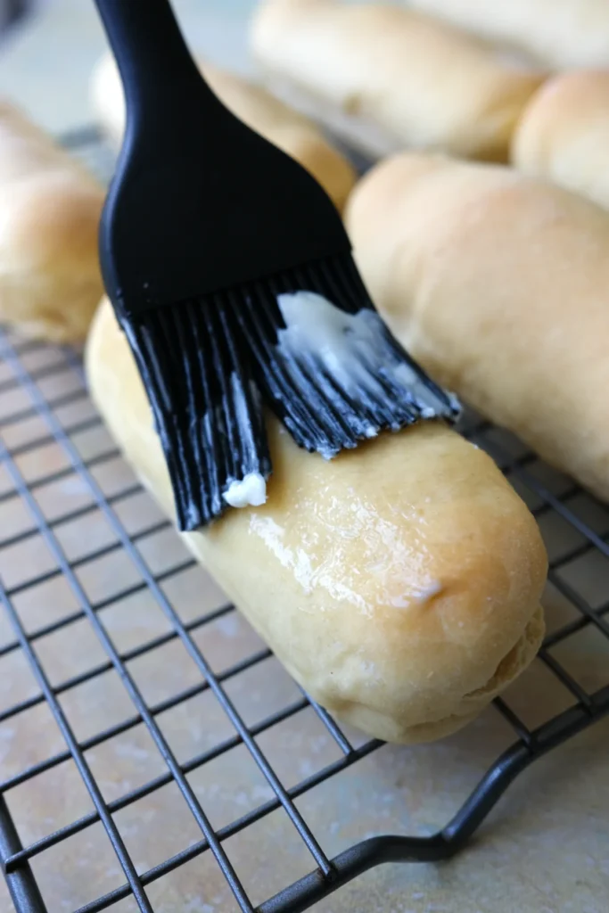 Brushing a freshly baked Filipino cheese roll with butter on a wire rack.