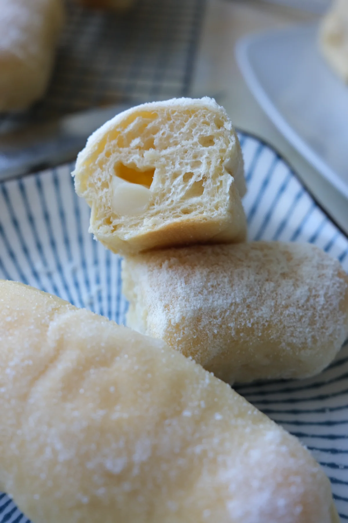 Filipino cheese rolls coated with sugar and milk powder, with one cut open to show the soft bread and cheese filling.
