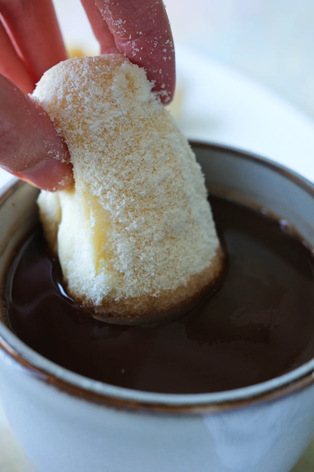 Milk powder-coated Filipino cheese roll being dipped into a cup of hot chocolate.