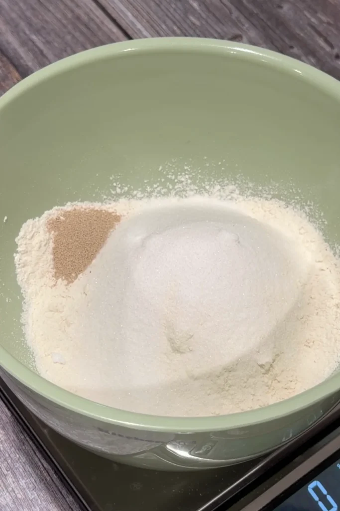 Flour, sugar, and yeast in a mixing bowl for homemade cheese roll dough.