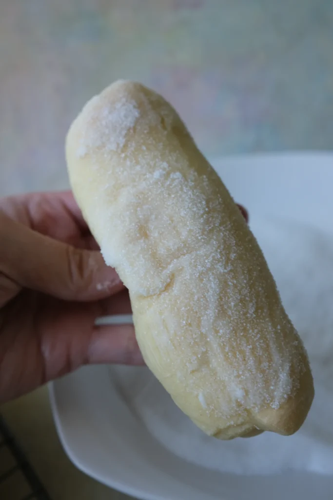 Filipino cheese roll coated in granulated sugar and held over a plate.