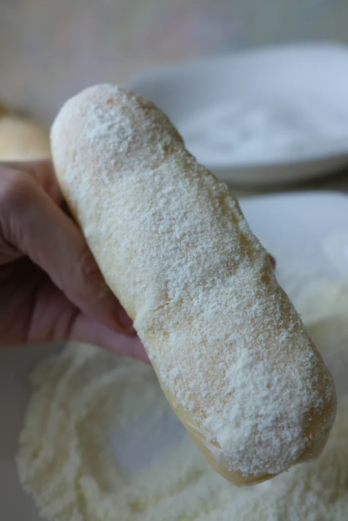 Freshly baked Filipino cheese roll coated in powdered milk and sugar mixture on a plate.