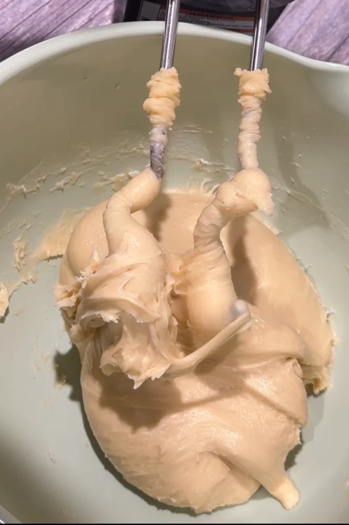 Soft, elastic cheese roll dough wrapped around the hooks of a hand mixer.
