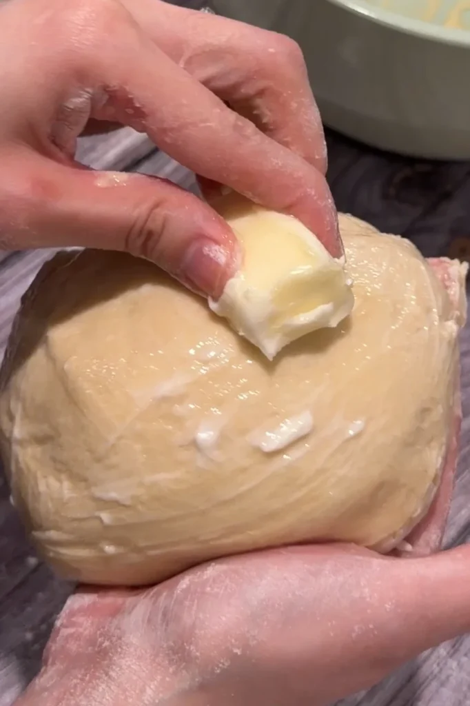 Rubbing softened butter over kneaded cheese roll dough.
