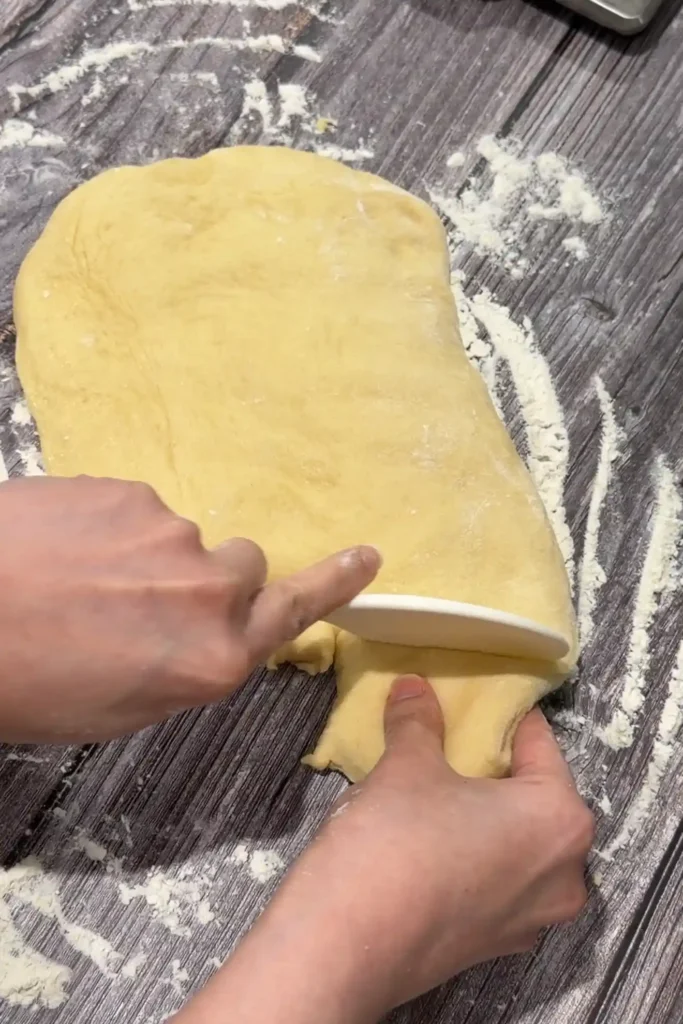 Dividing cheese roll dough into individual portions on a floured work surface.
