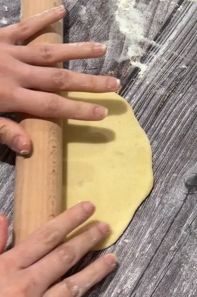 Rolling a portion of cheese roll dough into a thin oval.