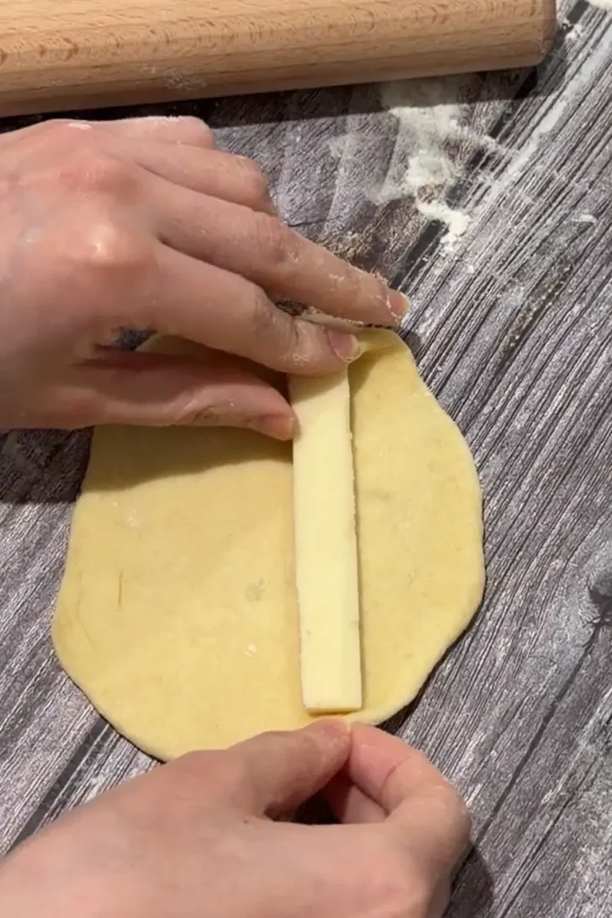 Placing a strip of cheese in the center of rolled cheese roll dough.