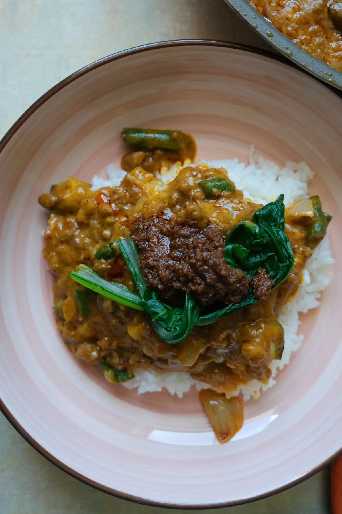 Overhead view of ground beef kare kare with rice, bok choy, and bagoong on a pink plate.