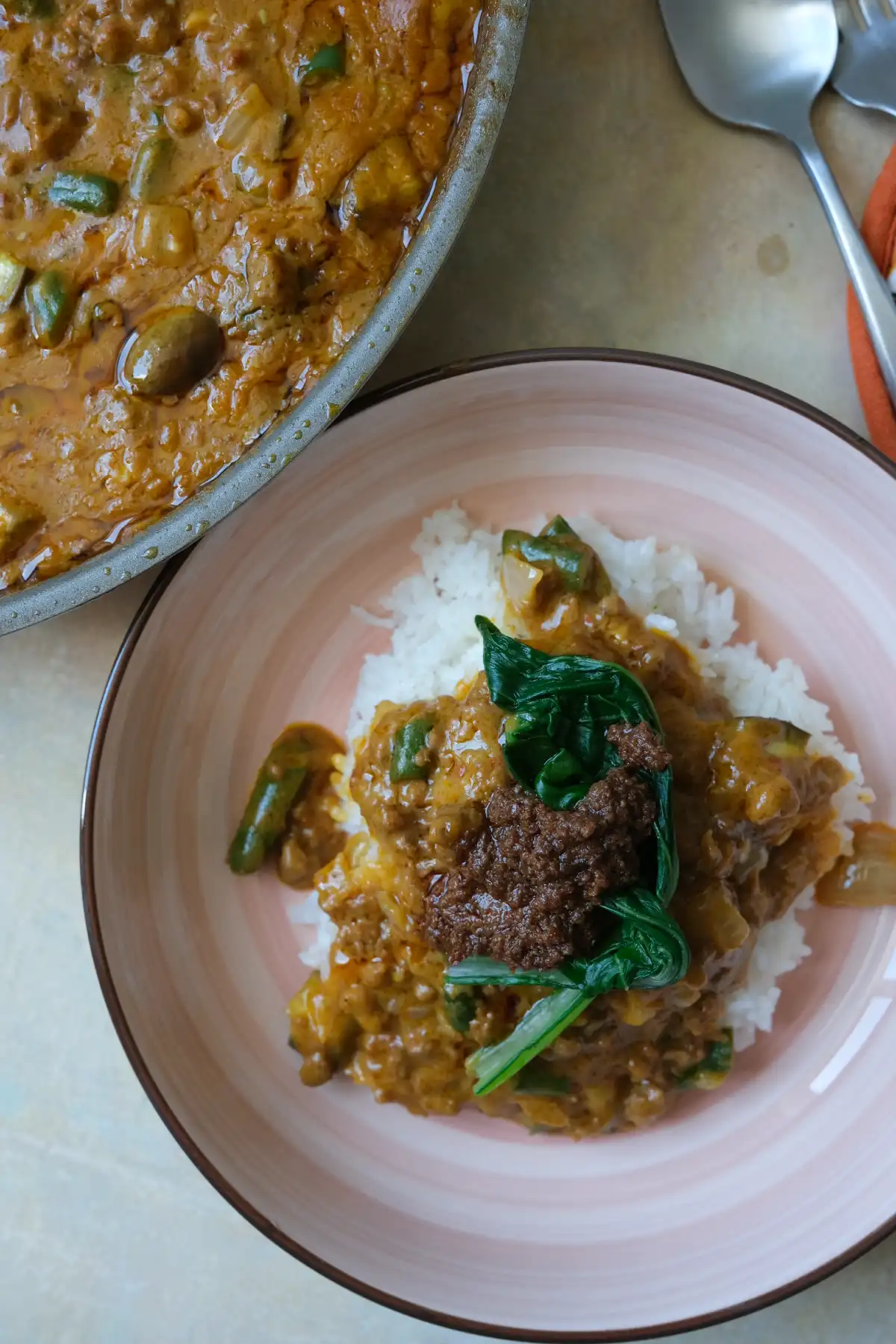 Ground beef kare kare served over rice with bok choy and bagoong, with the skillet in the background.