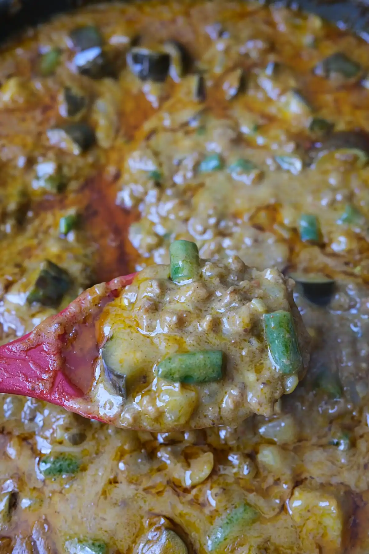 Spoonful of thick ground beef kare kare with eggplant and long beans in peanut sauce.