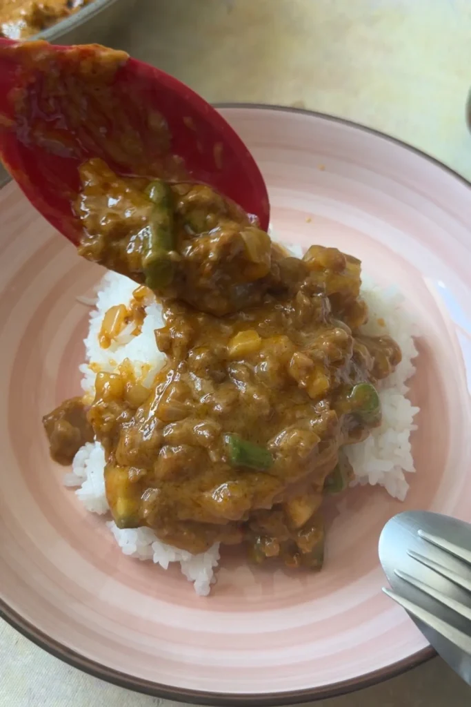 Ground beef kare kare being spooned over steamed white rice.