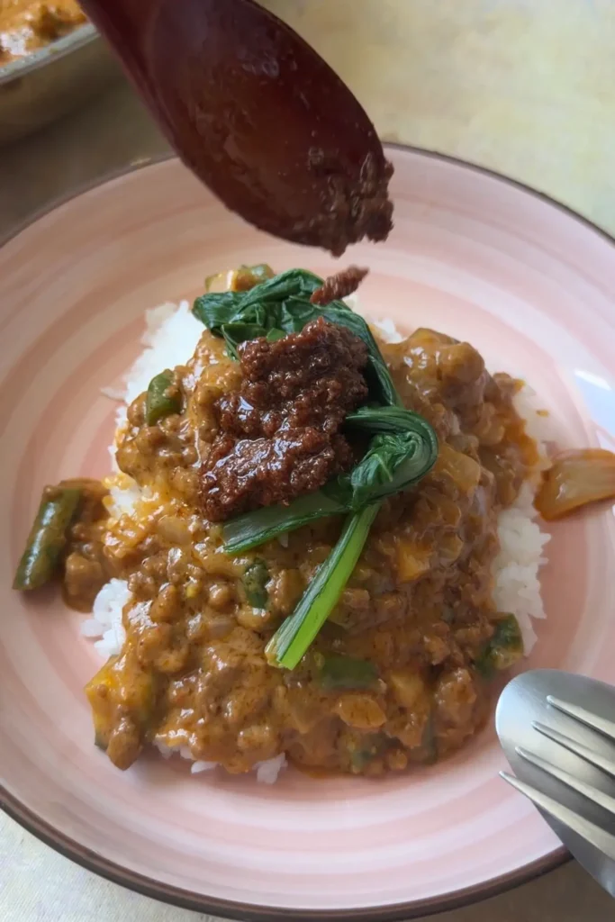 Bagoong being spooned over ground beef kare kare with bok choy and white rice.