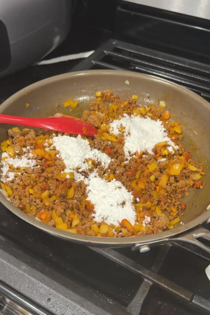 Cornstarch sprinkled over seasoned ground beef, onion, and garlic in a skillet.