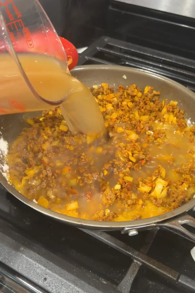 Beef broth being poured into the ground beef mixture.