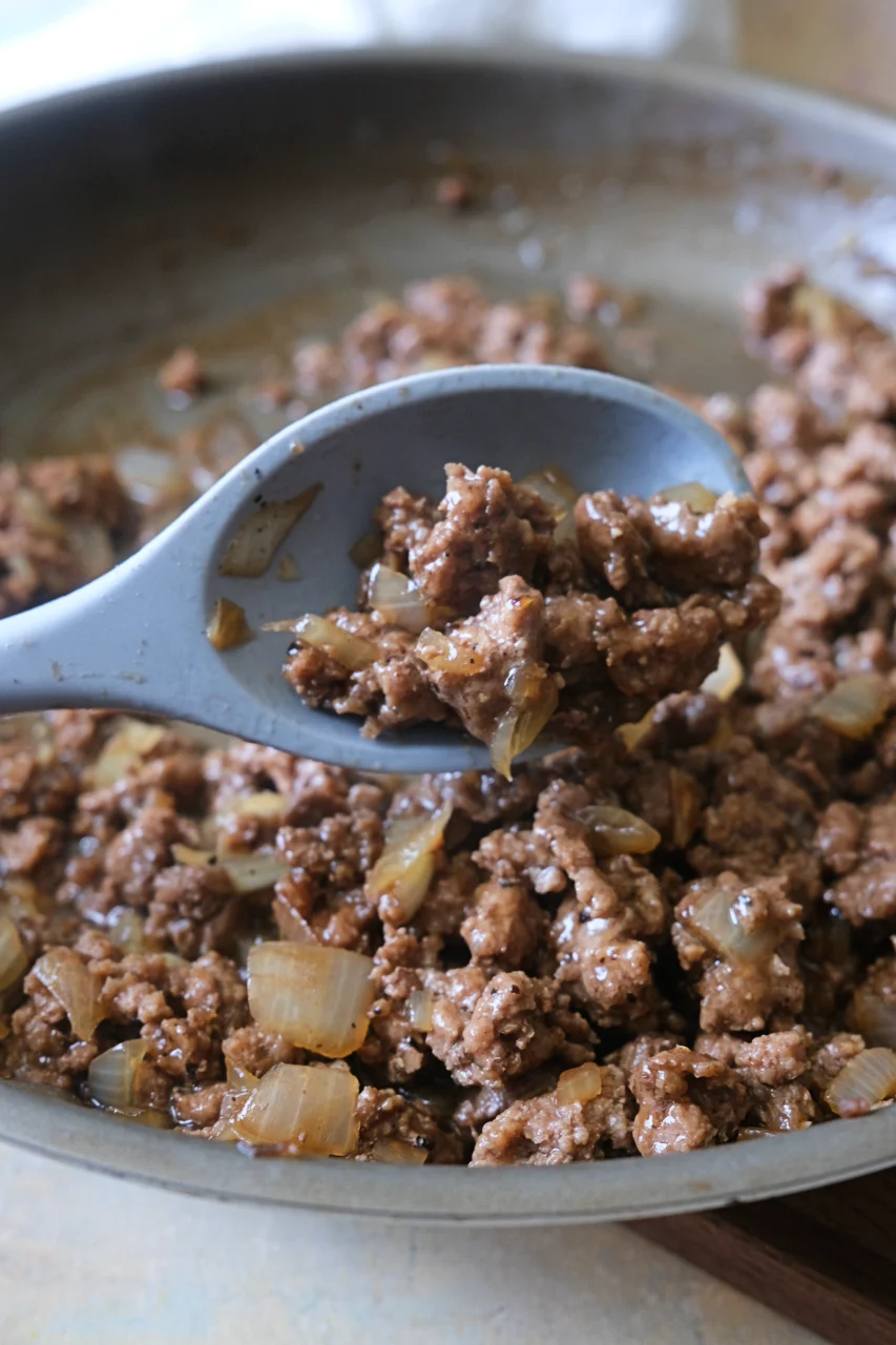 Spoonful of honey ground beef with onions held over the skillet.