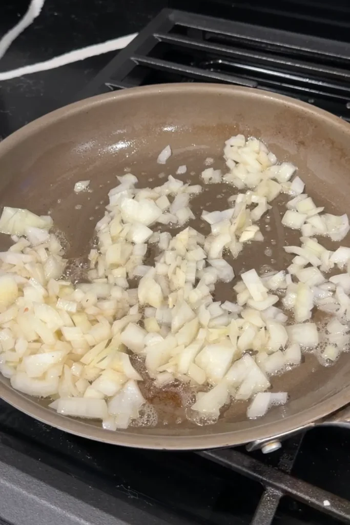 Diced yellow onions sautéing in melted butter in a skillet.
