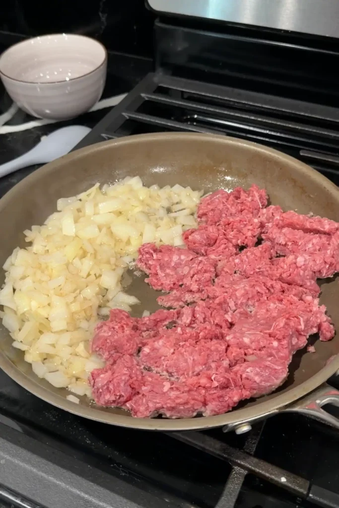 Ground beef added to sautéed onions in a skillet.