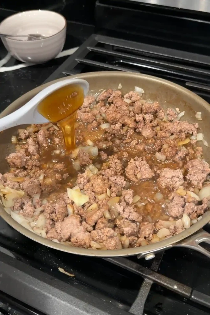 Honey and seasonings being added to cooked ground beef and onions.