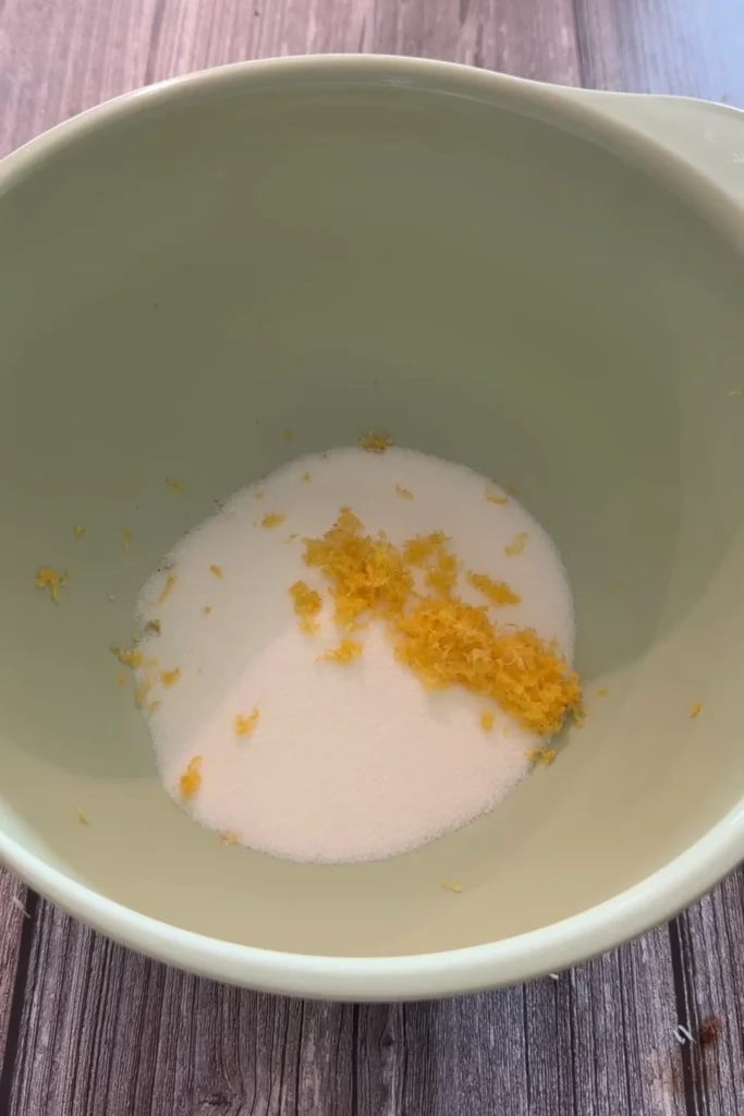 Granulated sugar and fresh lemon zest in a mixing bowl for invisible apple cake.