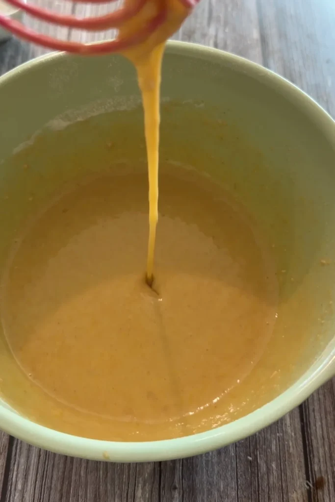 Smooth invisible apple cake batter dripping from a whisk.