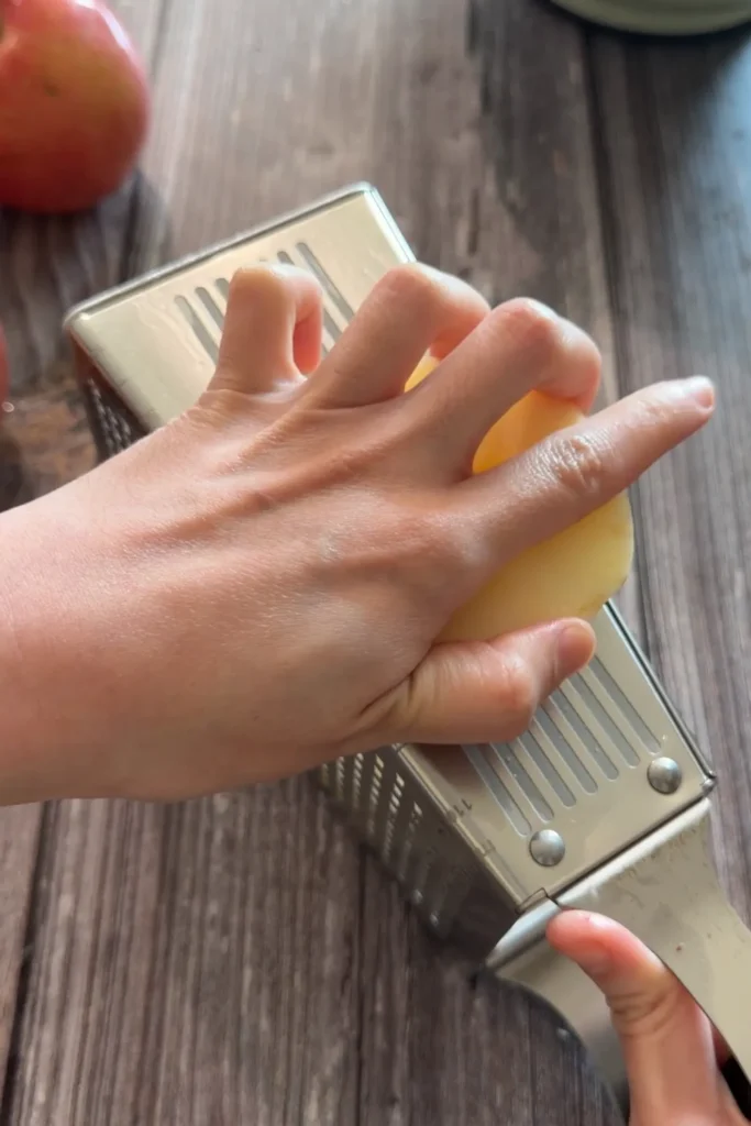 Peeled apple being thinly sliced using the mandoline side of a box grater.