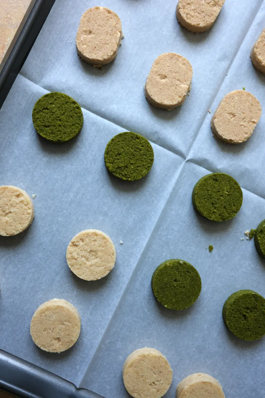 Classic and matcha Filipino polvoron arranged on a parchment-lined baking sheet.