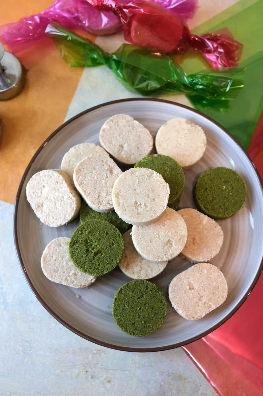 Classic, apple cinnamon, and matcha polvoron piled on a plate with colorful wrapped polvoron in the background.